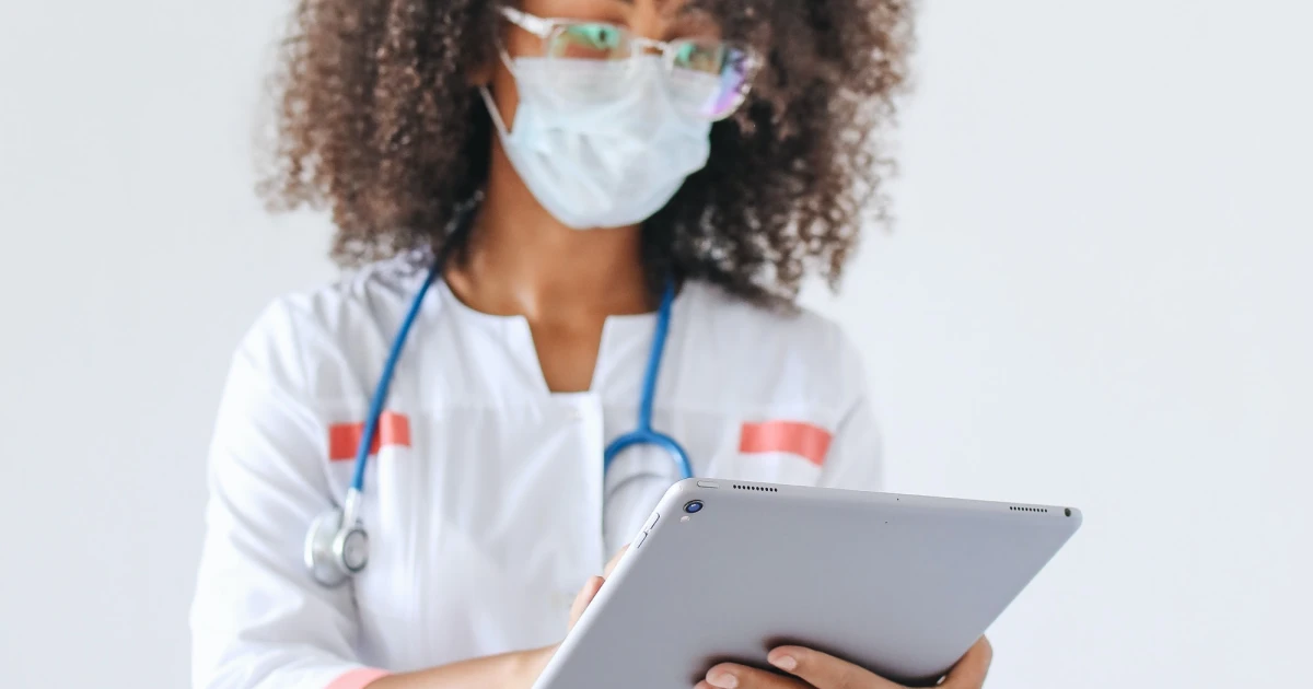 Healthcare worker in white scrubs looking down at tablet device.