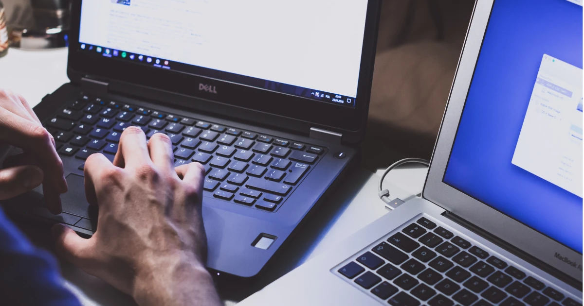 Two laptops sitting next to each other with person typing on one.
