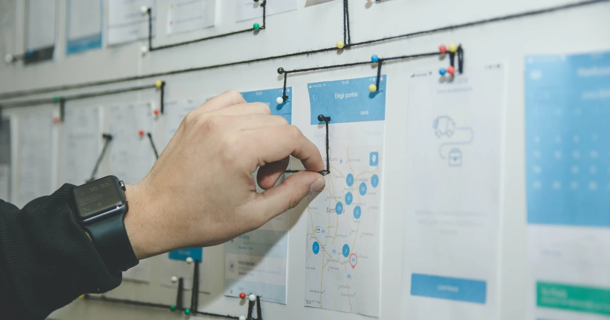 Hand connecting pins on a brainstorming board with pieces of string.
