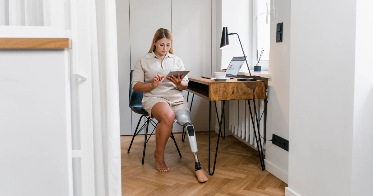 Young woman with prosthetic leg sitting at desk using tablet computer.