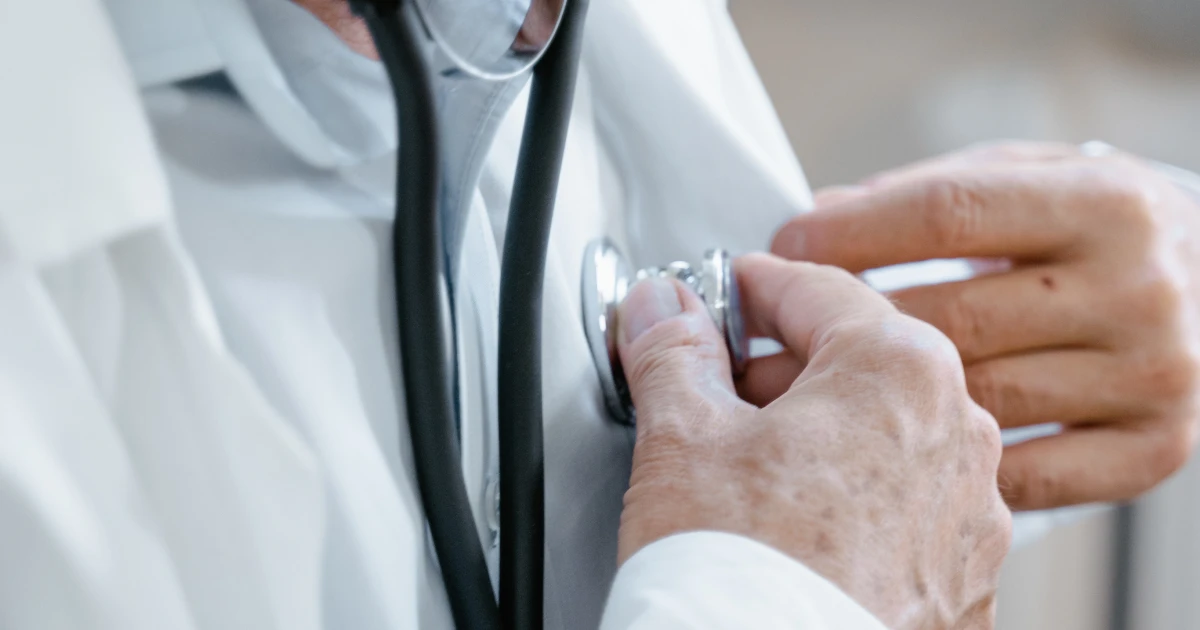 Physician wearing lab coat demonstrating how to check heartbeat using stethoscope.
