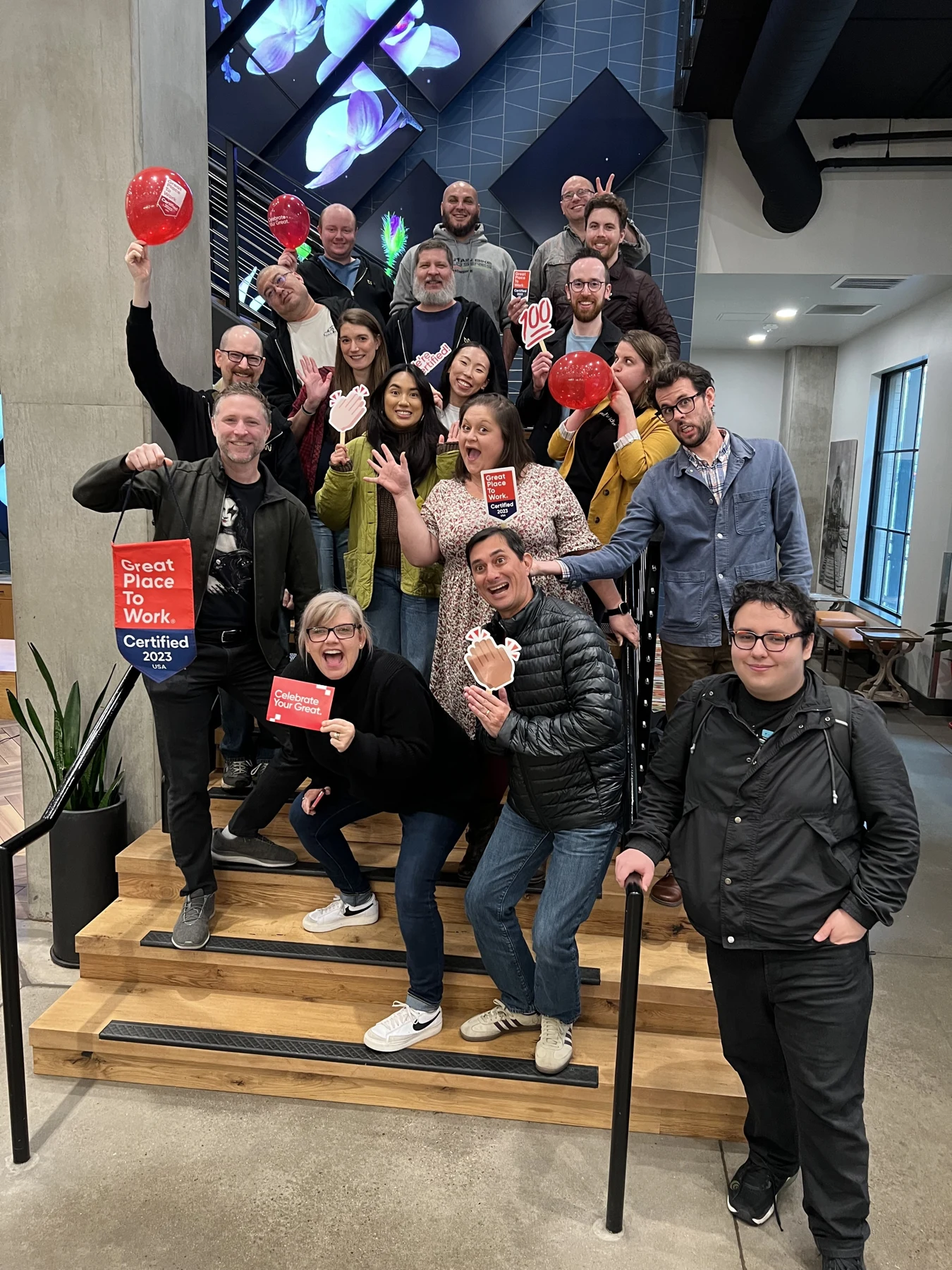 A group celebrating on the stairs with Great Place to Work signs