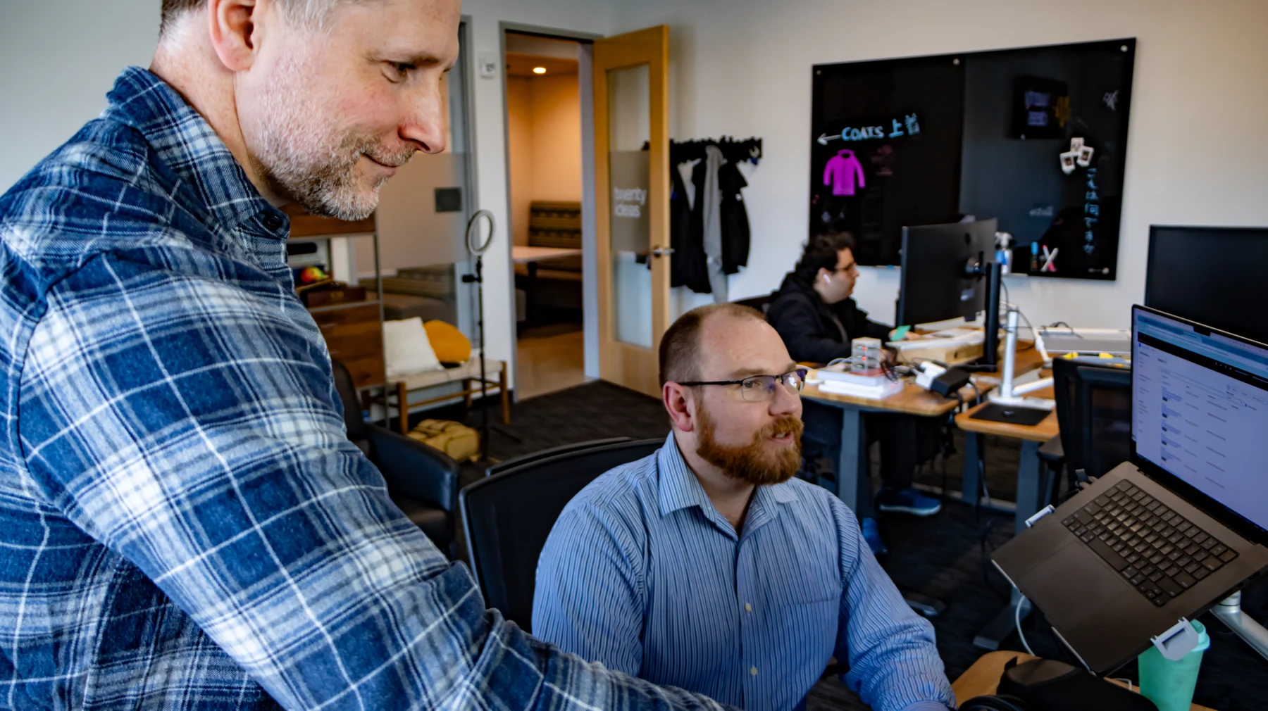 Two people reviewing work at a desktop monitor.